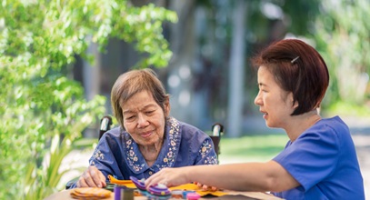 2 women working on a craft project together outside, one is in a wheelchair and one is in blue scrubs