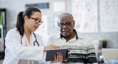 female healthcare worker wearing a white coat and stethiscope showing an older gentleman some notes on a pad