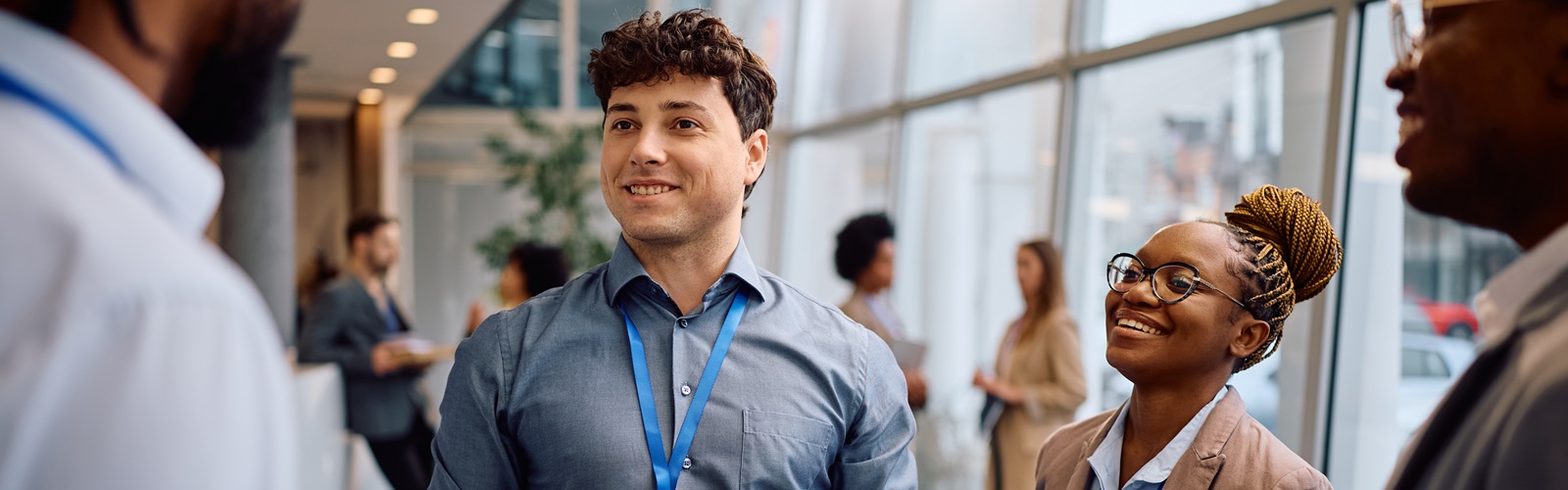 young man with curly brown hair and blue button-down shirts standing in a circle smiling at the other people