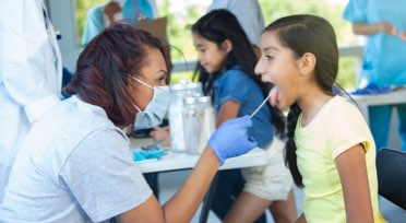 Healthcare worker swabbing child's tongue-alt-text