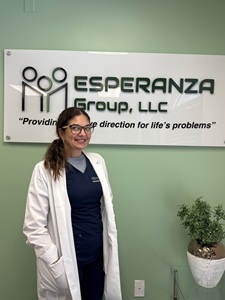 Daymi Martin standing in front of an Esperanza Group LLC sign in blue scrubs and a long white coat