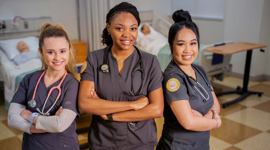 three nursing students in South University scrubs standing side by side in a classroom