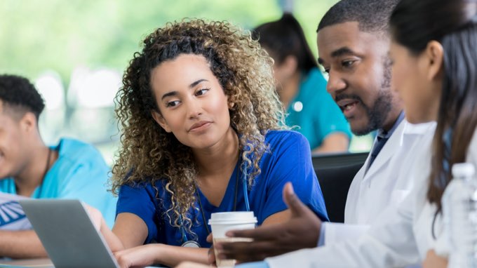 Female nursing student in classroom learning from instructor on laptop