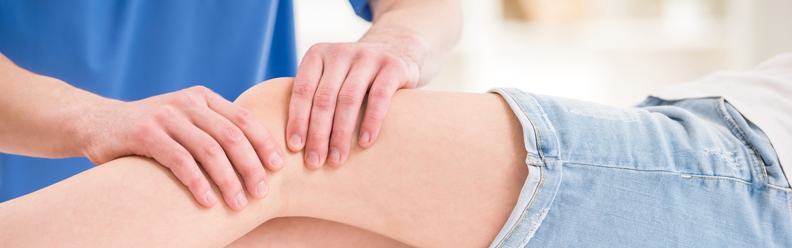 A healthcare worker in blue scrubs is massaging a patient's knee
