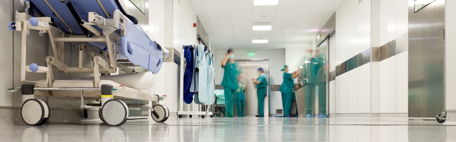 hospital hallway with a rolling hospital bed and severl staff in scrubs