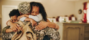 man in a military uniform wearing a backpack hugging 2 kids, one boy and one girl