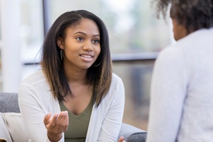 young african american woman in a white sweater sitting on a couch speaking to another person