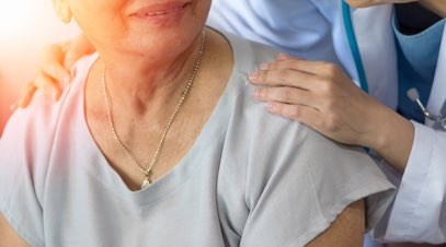 Nurse with hands on shoulders of older person smiling-alt-text
