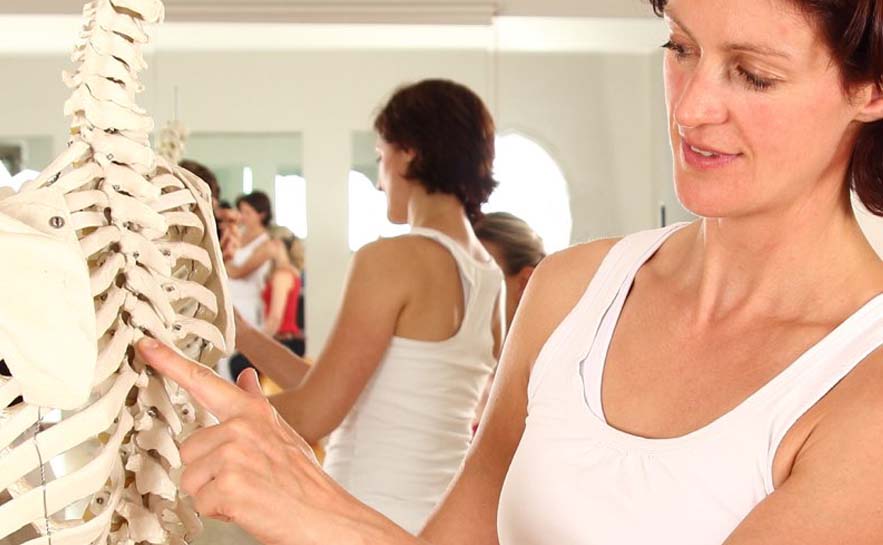 Woman in tank top pointing at a human skeleton model.