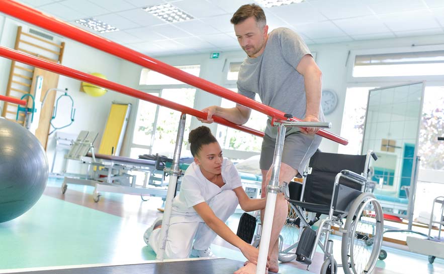 PTA working with man's leg while he holds on to balance bars