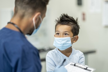 male healthcare personnel speaking with a young boy writing down information on a medical chart