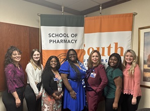Group of School of Pharmacy women posing in front of the school's logo
